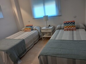 Ein Zimmer mit zwei Einzelbetten, einem Nachttisch mit Lampe und einem Fenster mit Jalousien.