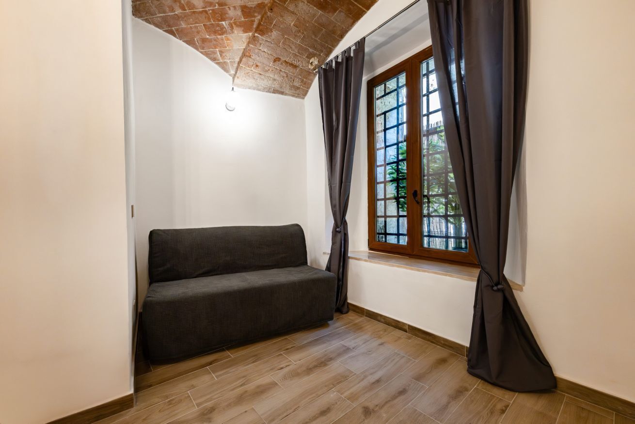 Una habitación con sofá, ventana con cortinas, techo de ladrillo y suelo de madera.