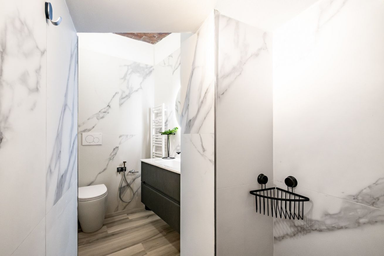 A modern bathroom with marble walls, a toilet, a sink, and a shower.