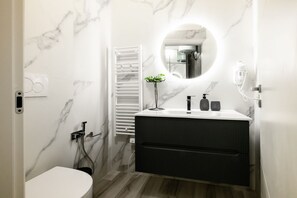 A modern bathroom with a marble wall, a round mirror, a white toilet, and a black vanity with a plant. - GuestHost - Porta Ovile Glam Home (Siena)