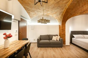 A room with a wooden dining table, a sofa, a bed, and a brick ceiling. - Elegant, fully renovated studio apartment sleeping up to 5 people, located in a period building just steps from Porta Ovile, one of the main entrances to the medieval heart of Siena. The area is well-served by all kinds of shops, and Piazza del Campo is  (Siena)