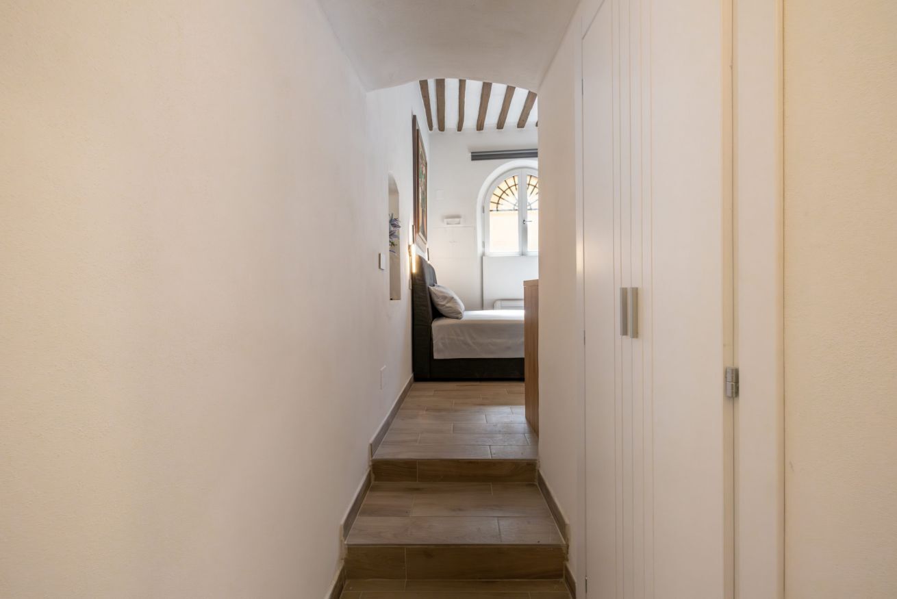 A narrow hallway with wooden steps leading to a bedroom with a bed and a window.