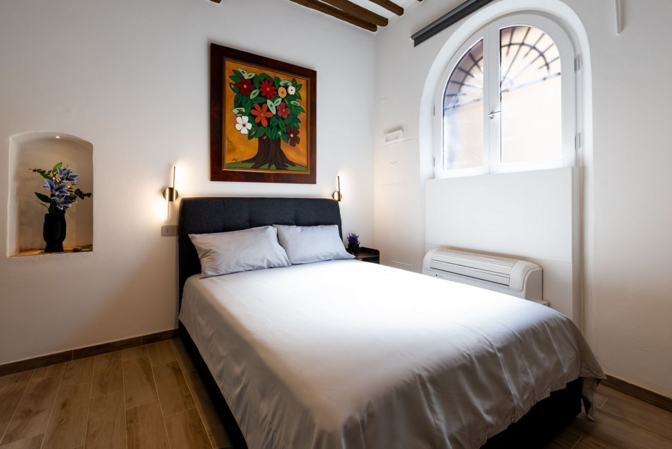 Ein Schlafzimmer mit Bett, einem an der Wand hängenden Bild, einem Fenster und einer Wandheizung.