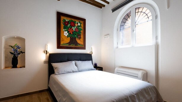A bedroom with a bed, a wall-mounted painting, a window, and a wall-mounted heater. - Charming studio apartment for two, renovated and located in a period building near Porta Ovile, one of the most convenient access points to the medieval heart of Siena. Its strategic location allows you to reach Piazza del Campo in about a 10-minute walk (Siena)