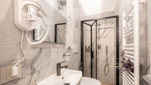 A modern bathroom with a marble sink, a toilet, a glass-enclosed shower, and a hairdryer on a wall socket. - Charming studio apartment for two, renovated and located in a period building near Porta Ovile, one of the most convenient access points to the medieval heart of Siena. Its strategic location allows you to reach Piazza del Campo in about a 10-minute walk (Siena)