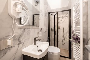 A modern bathroom with a marble sink, a toilet, a glass-enclosed shower, and a hairdryer on a wall socket. - Charming studio apartment for two, renovated and located in a period building near Porta Ovile, one of the most convenient access points to the medieval heart of Siena. Its strategic location allows you to reach Piazza del Campo in about a 10-minute walk (Siena)