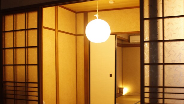 Una habitación japonesa tradicional con suelo de tatami, puertas correderas y una lámpara colgante.