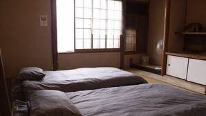 Una habitación con dos camas, una ventana, un ventilador y una repisa con una figurita de un animal.