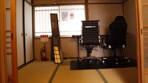 Una habitación con suelo de tatami, un escritorio con silla, una ventana con persianas, un extintor y una escalera.