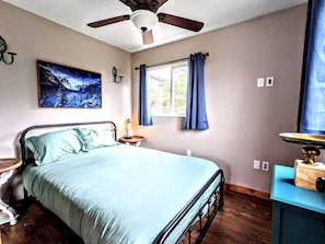 A bedroom with a bed, a ceiling fan, a window with curtains, a wall-mounted picture, and a bedside table. - 11 Luminous Lodge in Santa Ysabel, CA (Santa Ysabel)