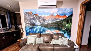 Una sala de estar con un sofá grande, una mesa de centro y un cuadro de un paisaje montañoso.