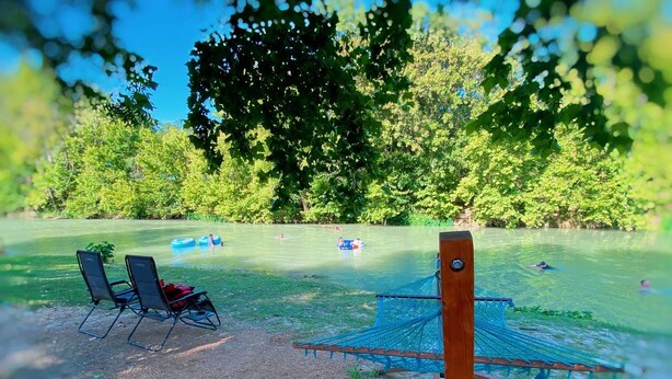 A hammock, two chairs, and a pool with people in the background. - Fun-Filled Glamping Adventure by the San Marcos River: Luxurious Safari Tent near Kingsbury, Texas, Perfect for Families (Kingsbury)