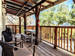 A covered outdoor deck with wooden furniture, a fire extinguisher, and a view of a river and trees. - Rustic Elegance by the Lake: Duplex Cabin Rental in Santa Ysabel (Santa Ysabel)