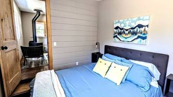 Un dormitorio con cama, mesita de noche, un cuadro y una puerta que da a otra habitación.