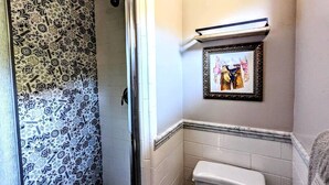Um banheiro com chuveiro, vaso sanitário e um quadro na parede.
