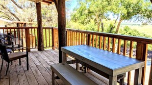Um deck de madeira ao ar livre com uma mesa de piquenique e bancos, cercado por árvores e vista para a paisagem.