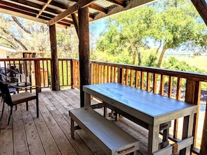 An outdoor wooden deck with a picnic table and benches, surrounded by trees and a view of the landscape. - Rustic Elegance by the Lake: Duplex Cabin Rental in Santa Ysabel (Santa Ysabel)