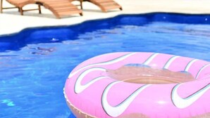 En pool med solstolar och en rosa uppblåsbar badring.