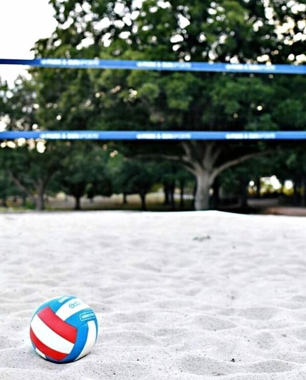 A volleyball on a sandy surface with blue tape and trees in the background.