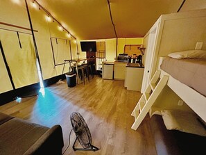 Ein kleines Zimmer mit Etagenbett, einer Küchenzeile, einer Essecke und einem Ventilator.