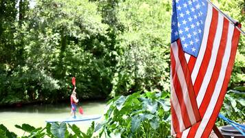 A kayaker on a river, surrounded by lush greenery and an American flag.