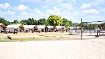 A row of tents with picnic tables and barbecue grills, set against a backdrop of trees and a clear sky.