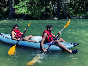 Two people kayaking on a river surrounded by trees.