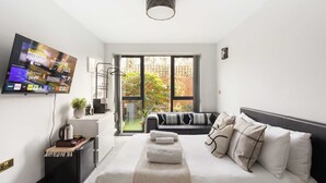 Een moderne hotelkamer met een grote televisie, een bed met veel kussens, een klein bijzettafeltje en uitzicht op het buitengebied via een schuifdeur.