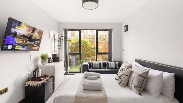 Een moderne hotelkamer met een bed, een aan de muur bevestigde televisie, een raam met uitzicht op groen en een klein tafeltje met een waterkoker.