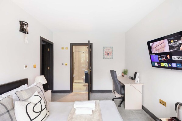 A hotel room with a bed, a desk, a TV, and a door leading to a bathroom.