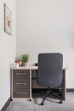 Un escritorio con una silla, una planta y un cuadro en la pared.
