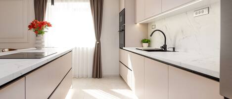 A modern kitchen with a marble countertop, a built-in oven, a sink, and a pendant light.