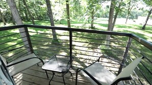Een terras met twee metalen stoelen en een kleine tafel, omgeven door een metalen hekwerk, met uitzicht op een grasveld met bomen.