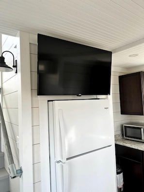 A kitchen with a white refrigerator, a microwave, and a flat-screen TV mounted above the fridge.
