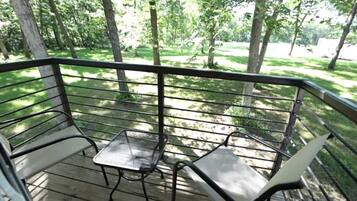 Un terrazzo con due sedie in metallo e un tavolino, circondato da un parapetto metallico, affacciato su una zona verde con alberi.