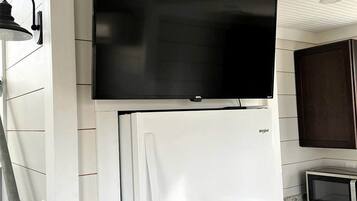 Ett kök med ett vitt kylskåp, en mikrovågsugn och en platt-TV som är monterad ovanför kylskåpet.