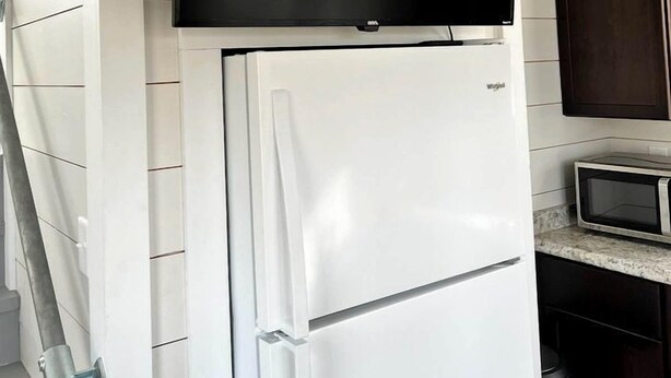 Een keuken met een witte koelkast, een magnetron en een flatscreen-tv die boven de koelkast is bevestigd.
