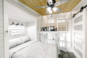 Un dormitorio con literas, ventilador de techo, ventana y mesita de noche.