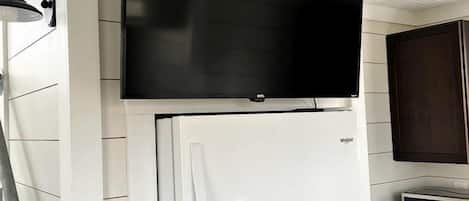 A kitchen with a white refrigerator, a microwave, and a flat-screen TV mounted above the fridge.