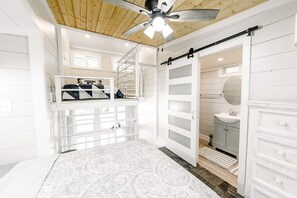 A spacious room with a bunk bed, a ceiling fan, a sliding door, and a bathroom with a sink and mirror.
