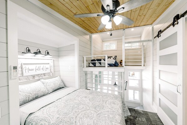 Une chambre avec un lit superposé, un ventilateur de plafond, une fenêtre et une table de chevet.