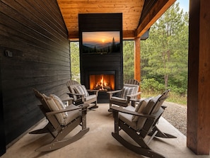 Eine Holzhütte mit Kamin, Schaukelstühlen und Blick auf einen Wald.