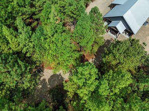 An aerial view of a forested area with a building that has a sloped roof and a chimney. - Twisted Leaf Luxury Cabin | Hot Tub | Wooded Walking Trail (Broken Bow)
