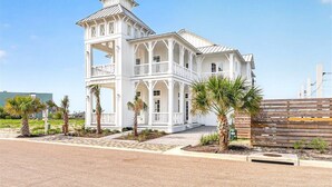 Un edificio blanco de varios pisos con balcón, palmeras y entrada empaveda.