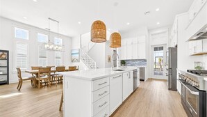 Una cocina moderna con armarios blancos, una isla central, electrodomésticos de acero inoxidable y un comedor con mobiliario de madera.
