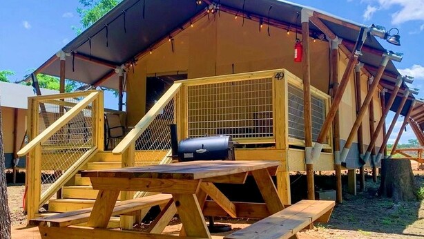 Een houten constructie met een overdekte patio, een barbecue en een omheind toegangshek.
