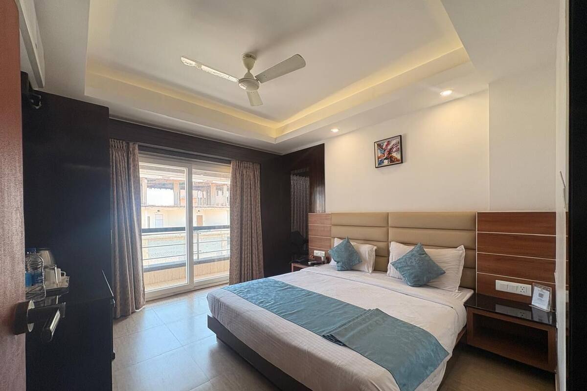 A hotel room with a bed, bedside table, a ceiling fan, a window with curtains, and a view of the outside.