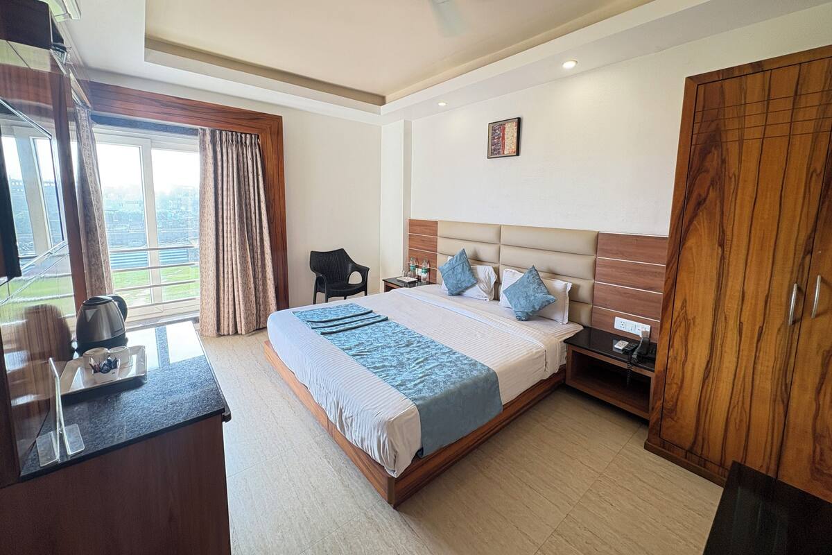 A hotel room with a large bed, a desk with a kettle, a chair, and a wardrobe.
