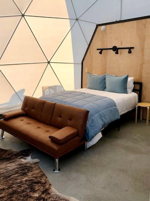 Un dormitorio con una cama, un sofá marrón, una mesita y un diseño geométrico en la pared.