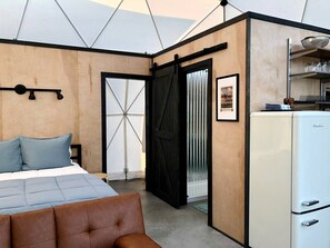 Un dormitorio con cama, cómoda, refrigerador blanco y puerta que da a un balcón.